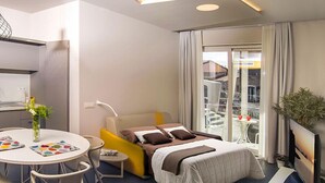 Una habitación de hotel moderna con cama, zona de comedor, televisión y balcón con vistas.