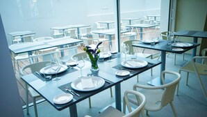 Un área de comedor al aire libre con mesas dispuestas para dos, cada una con platos, cubiertos y vasos.