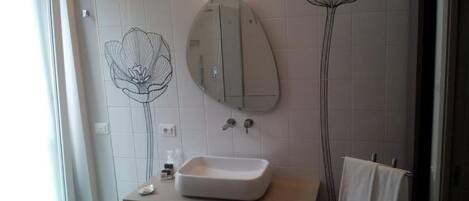 A bathroom with a white sink, a mirror, and wall art depicting flowers.
