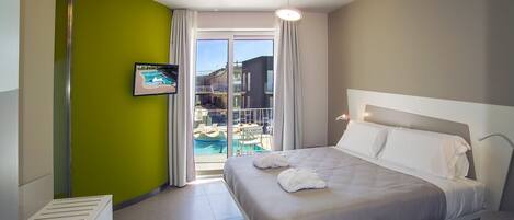 A hotel room with a bed, a TV, and a view of a pool and building.