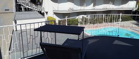 A balcony with a pool, white railings, and a table with a chair.