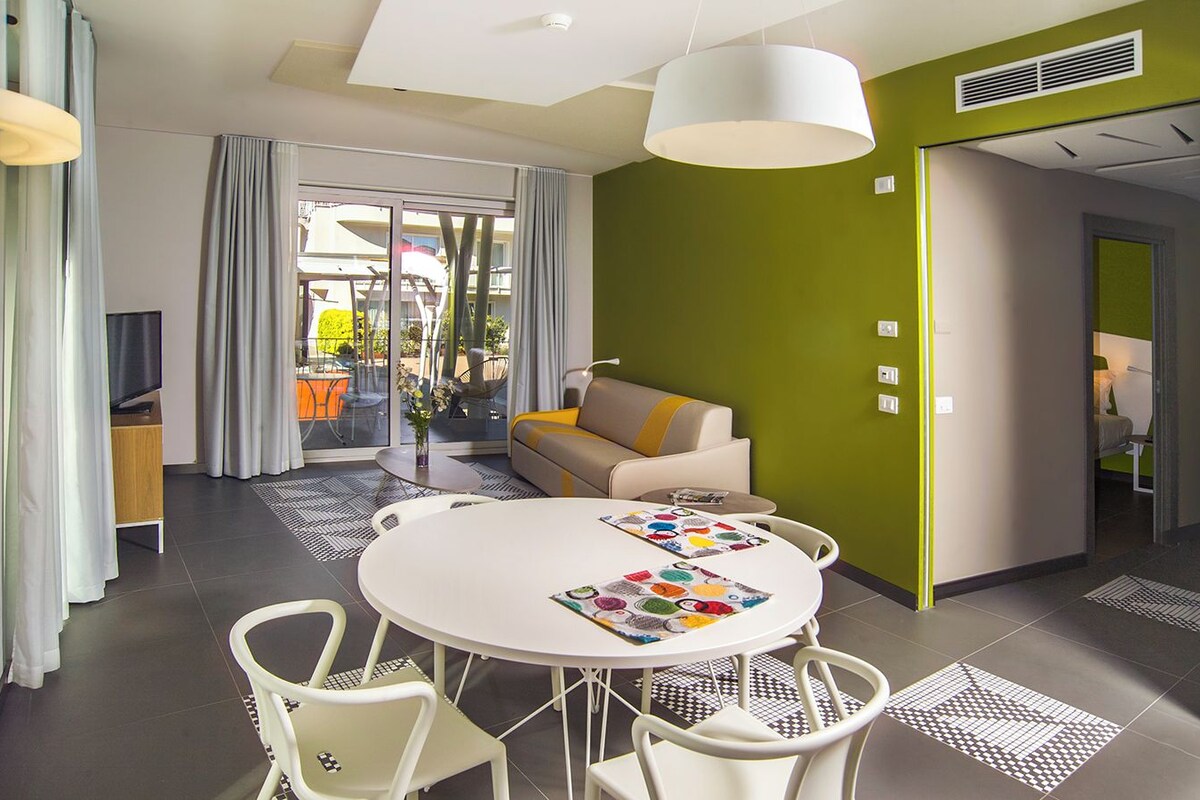 Una habitación de hotel moderna con comedor, sofá y televisor.