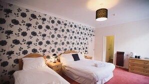 A hotel room with two single beds, a wooden headboard, bedside tables with lamps, a red carpet, a wardrobe, and a floral wallpaper. - Bowmans Hotel (Goole)