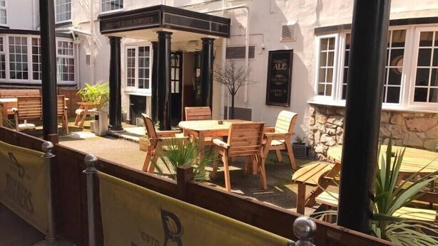 An outdoor seating area with wooden tables and chairs, a stone wall, and a sign reading "WELCOME TO THE BOWMAN'S". - Bowmans Hotel (Goole)