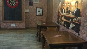 A room with a dartboard, a framed picture of a drink, and a mural of a poker game. - Bowmans Hotel (Goole)