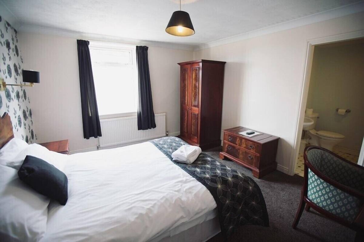 A hotel room with a bed, a wardrobe, a desk, and a chair.