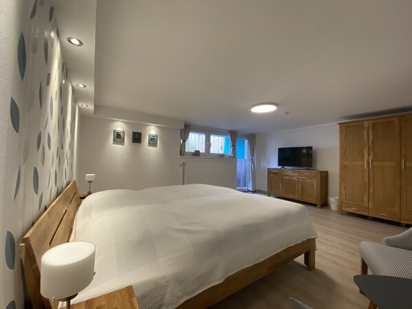 A bedroom with a large bed, wooden wardrobe, a television, and a window with curtains.