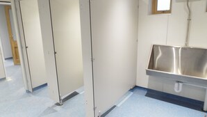 Des toilettes avec trois cabines, un évier en acier inoxydable et une fenêtre située au-dessus.