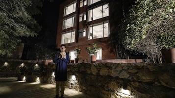 A person standing in front of a building with multiple windows and potted plants.
