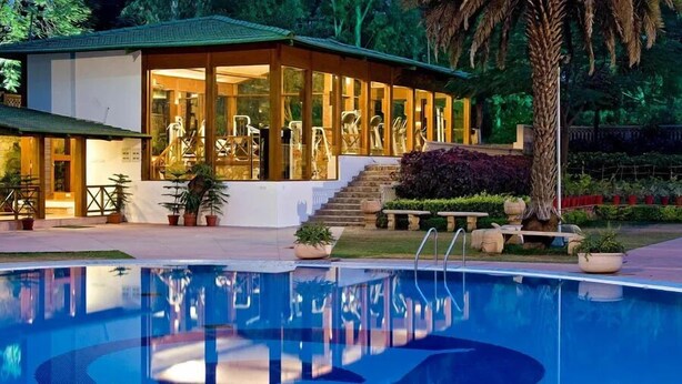 Un edificio junto a la piscina con fachada de vidrio, mobiliario exterior y una escalera que conduce a una terraza.