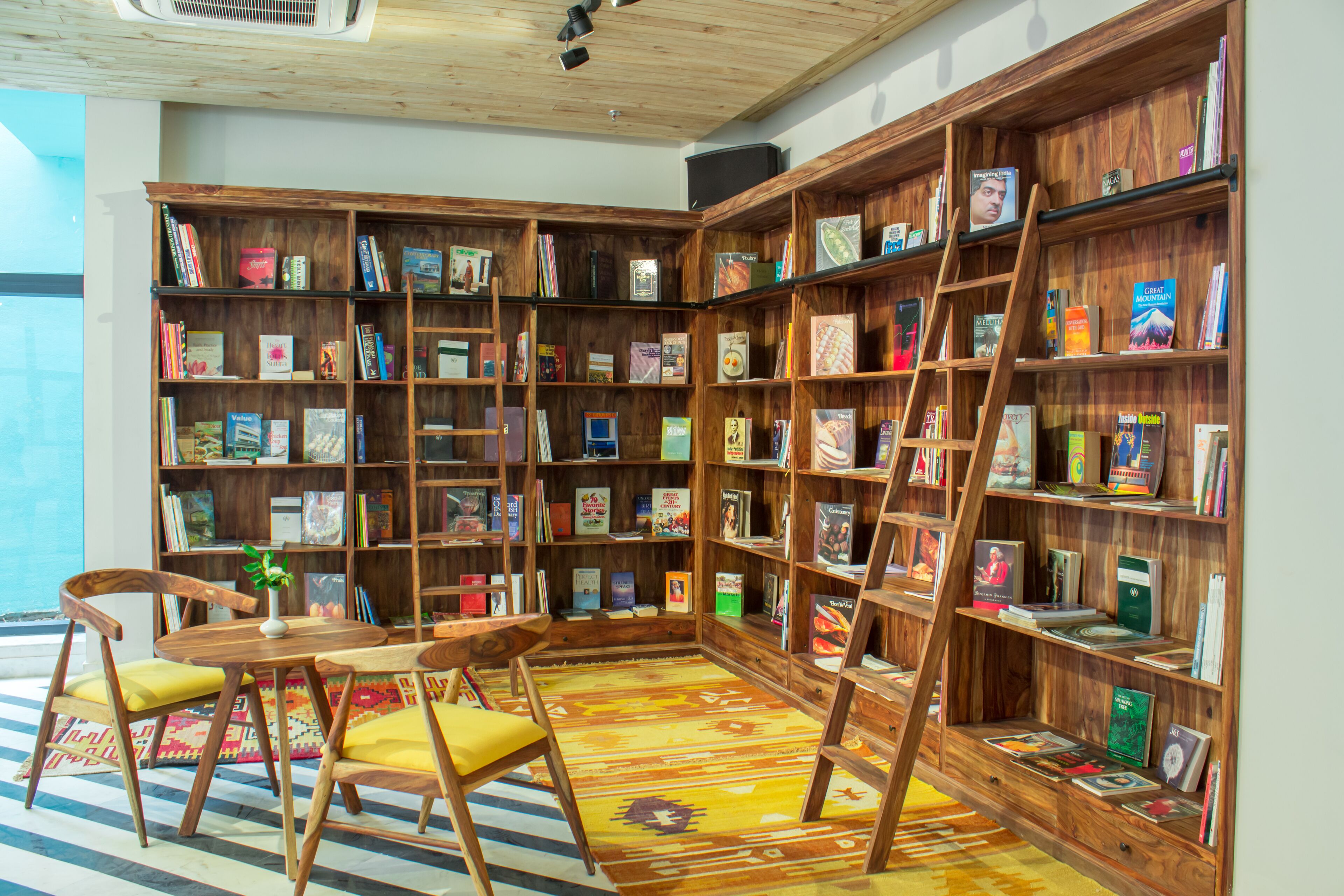 A cozy reading nook with wooden bookshelves, a small table, chairs, and a colorful rug.
