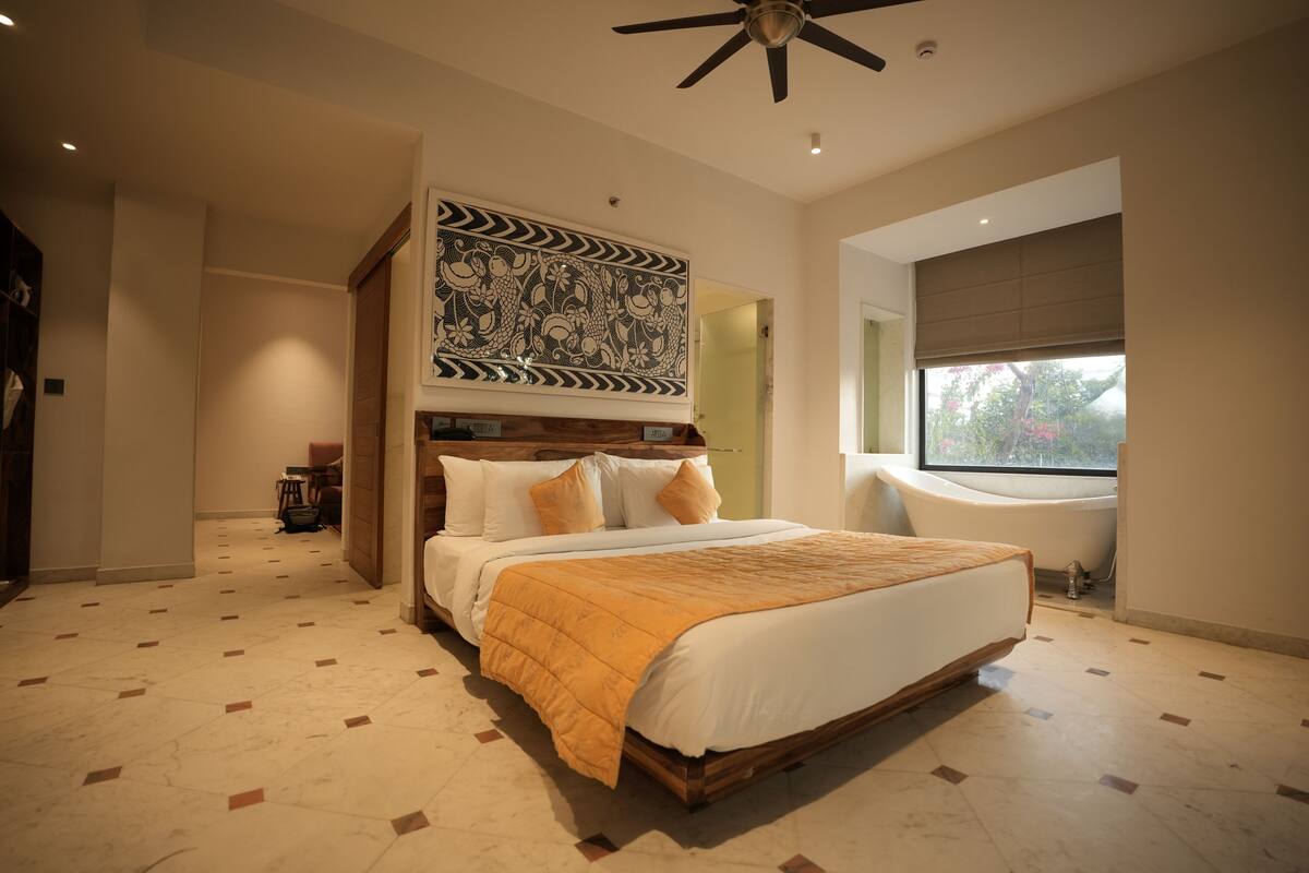 A spacious bedroom with a large bed, a ceiling fan, a window with a view, and a decorative wall piece.