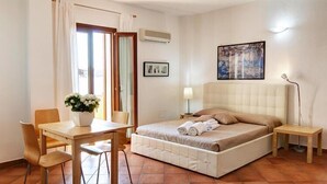 Un dormitorio con cama, mesita de noche, lámpara, silla, mesa y ventana con cortinas.