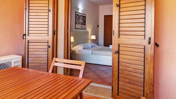 Una habitación con cama, una mesa y sillas, y contraventanas de madera en las puertas.