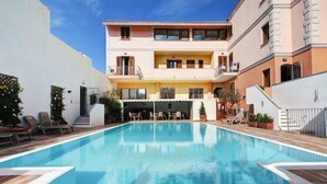 Una piscina con sillones de descanso y un edificio con balcones.
