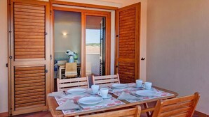 Un comedor con una mesa dispuesta para cuatro personas, contraventanas de madera y vistas al exterior.