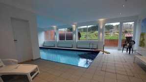 Une piscine avec vue sur un mur de briques et un espace verdoyant à l’extérieur. On y trouve des chaises et une table près de la piscine.