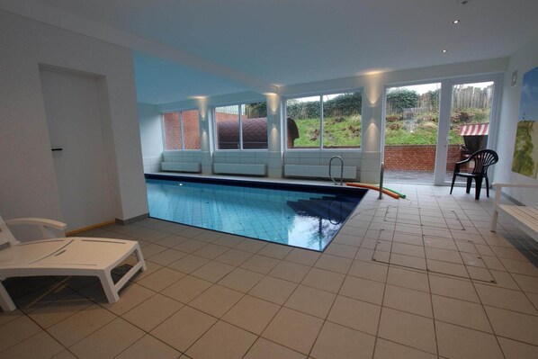 Una piscina con vistas a un muro de ladrillo y una zona verde exterior. Hay sillas y una mesa cerca de la piscina.