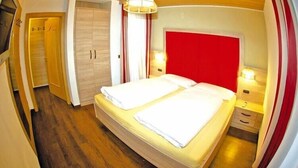 Un dormitorio con dos camas, cabecera roja, suelo de madera y un armario.