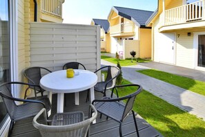A deck with a round table and four chairs, a small yellow object on the table, and a pathway leading to a building with balconies. - Large holiday homes, swimming pool, jacuzzi (Ustronie Morskie)