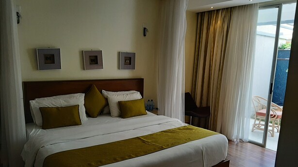 A hotel room with a large bed, a wooden headboard, and a view of the outdoor area through a glass door. - Executive D2W suites and residences (machakos)