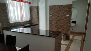 A modern kitchen with a central island, a dining area with dark wooden chairs, and a bathroom with a mirror and sink. - Executive D2W suites and residences (machakos)