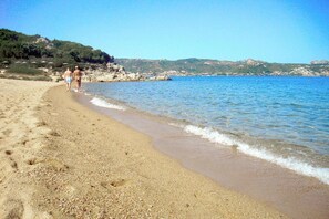 A beach with clear water, a sandy shore, and a few people walking.