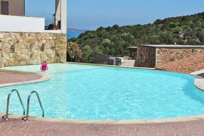 A swimming pool with a stone wall and a view of the sea.