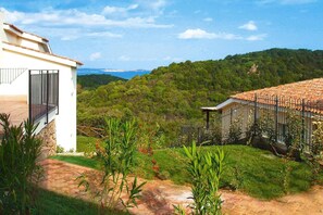 A residential property with a white building, a fenced garden, and a view of a forested hill.