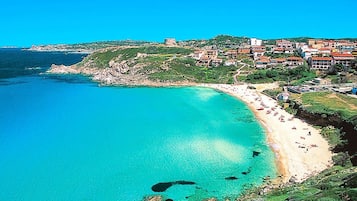 Ein Küstenort mit einem Sandstrand, klarem türkisblauem Wasser und Häusern mit roten Dächern.
