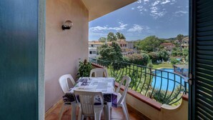 Ein Balkon mit Tisch und Stühlen, mit Blick auf einen Swimmingpool und Wohnhäuser.