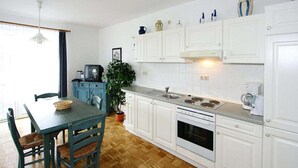 A compact kitchen with white cabinets, a dining table with chairs, a potted plant, and a television.