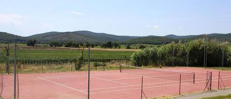 Un court de tennis entouré de champs verdoyants et de collines.
