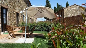 Un edificio de piedra con un patio que incluye una mesa, sillas, un parasol grande y un jardín bien cuidado.