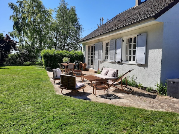 Una casa con un patio amoblado al aire libre, que incluye mobiliario, una hamaca y un jardín.