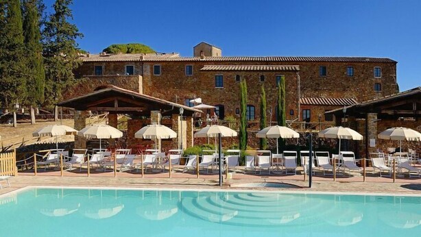 A pool area with lounge chairs and umbrellas, a stone building in the background, and a clear blue sky. - Apartment in Campiglia Marittima (Campiglia Marittima)