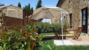 A stone building with a patio area featuring a table and chairs, a large umbrella, and a well-maintained garden. - Apartment in Campiglia Marittima (Campiglia Marittima)