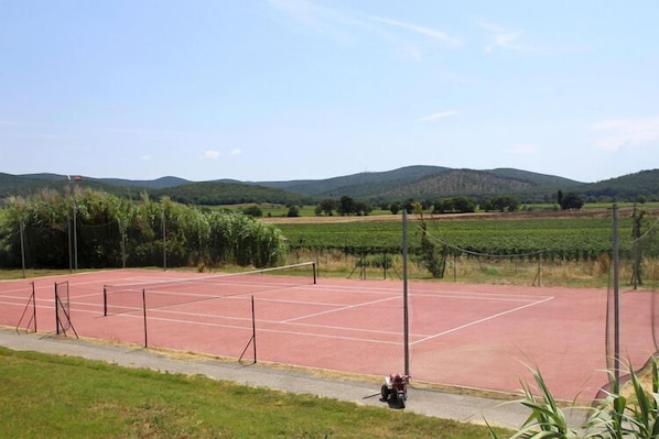 Un campo da tennis all'aperto circondato da campi verdi e colline.