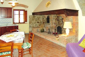 Ein Essbereich mit einem Tisch für zwei Personen, einem Kamin aus Stein und einer Küche im Hintergrund.