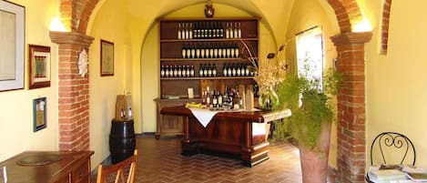 A wine cellar with a brick archway, wooden shelves with wine bottles, a bar area with a counter, and a potted plant.
