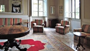 Un salon spacieux avec une table ronde en bois, des fauteuils à rayures et un tapis rouge à motifs.
