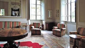 Un salón amplio con una mesa redonda de madera, sillones a rayas y una alfombra roja estampada.