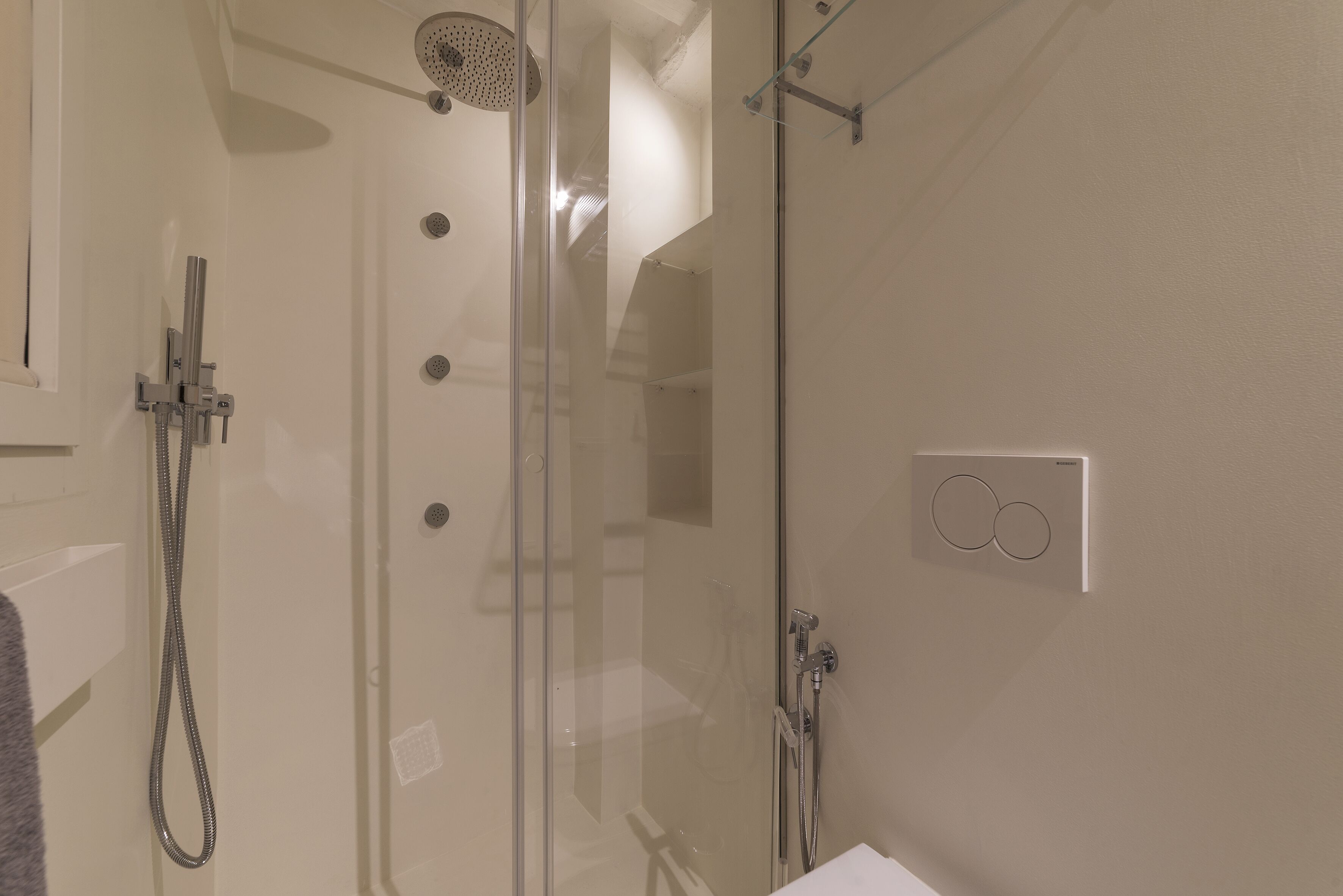 A modern shower with a glass enclosure, a handheld showerhead, and a wall-mounted control panel.