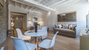 A modern living room with a dining area, featuring a white table with chairs, a sofa, and a painting on the wall.
