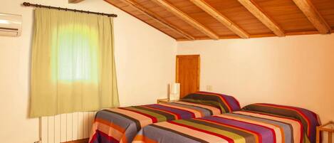 Una habitación con dos camas, una ventana con cortina, un radiador y techo de madera.