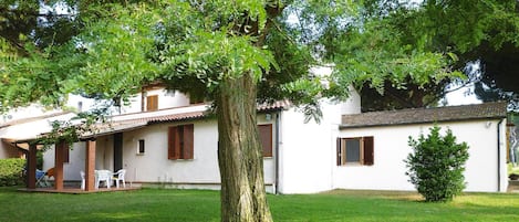 Un edificio blanco con un árbol grande en el frente, un porche cubierto y un pequeño jardín.