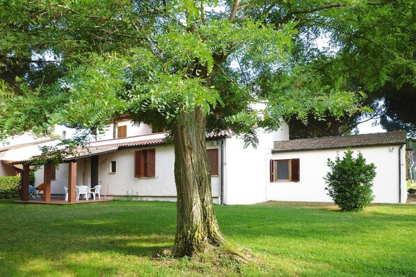 A white building with a large tree in front, a covered patio, and a small garden.