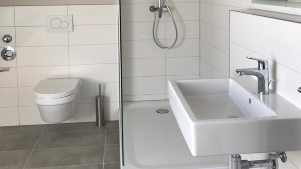 A modern bathroom with a glass-enclosed shower, a white toilet, and a white sink with a mirror above it. - TH39 Trend Hotel (Bad Vilbel)