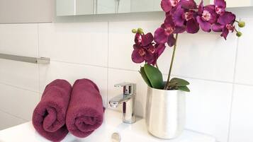 Un baño con lavamanos blanco, espejo y orquídea en maceta.