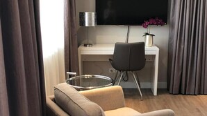 A modern hotel room with a sofa, a desk with a flat-screen TV, a lamp, and a potted plant. - TH39 Trend Hotel (Bad Vilbel)